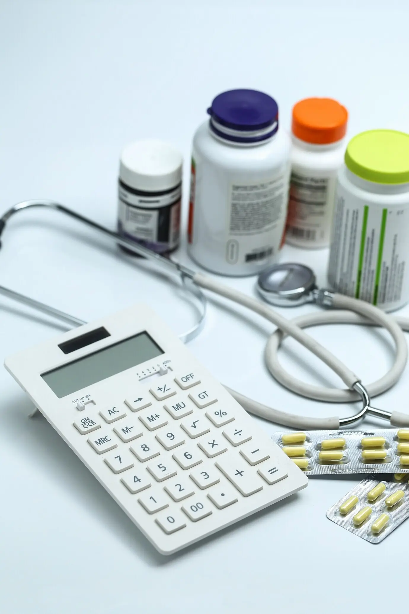 A calculator, a stethoscope, and medicine bottles on a white background.