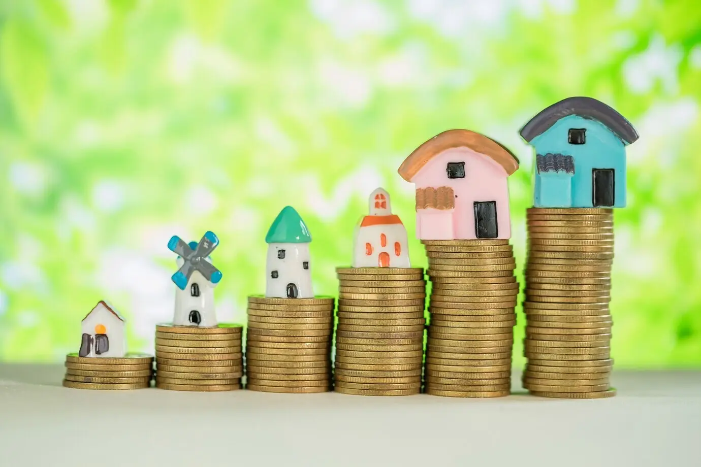A miniature house atop a stack of coins with a green blur.